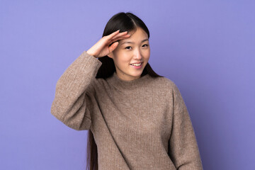 Young asian woman isolated on purple background looking far away with hand to look something