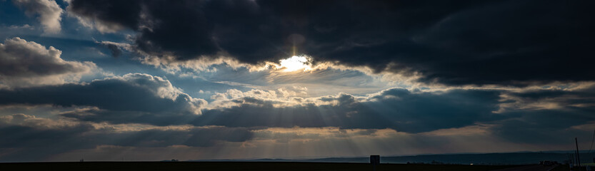 Panorama d'un couché de soleil perçant à travers les nuages avec ses rayons en pleine campagne...