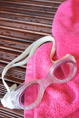 Swim goggles and pink towel on wooden deck