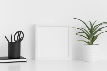 White square frame mockup with a aloe vera in a pot and workspace accessories on a white table.