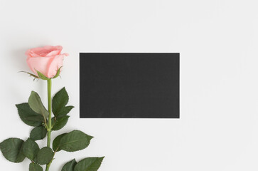Top view of a black card mockup with a pink rose on a white table.
