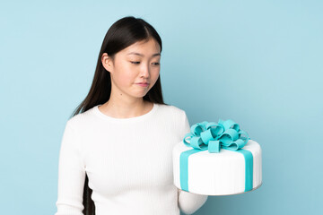 Pastry asian chef holding a big cake isolated on blue background with sad expression