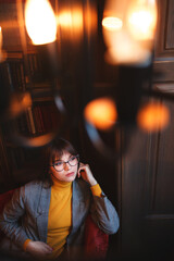 Beautiful dreamy girl in stylish sharp glasses. In the library.