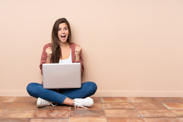 Teenager student girl sitting on the floor with a laptop celebrating a victory in winner position