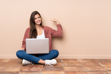 Teenager student girl sitting on the floor with a laptop doing strong gesture