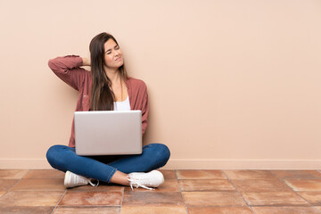 Teenager student girl sitting on the floor with a laptop with neckache