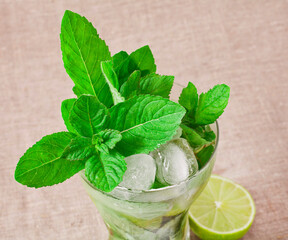 Cocktail mojito with mint leaves, lime and ice on a textile background.