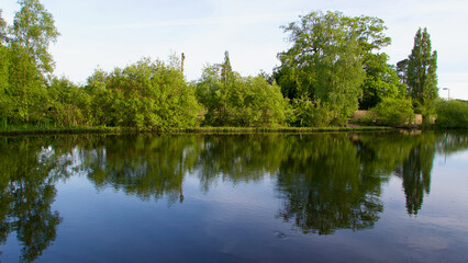 Fototapeta na wymiar Beautiful English village pond with trees and bushes reflected in still water