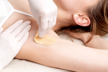 Hand of cosmetologist applying wax paste on armpit. Depilation or epilation female armpit with...