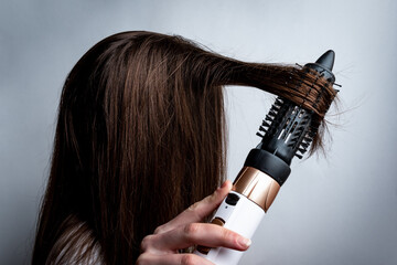 Fototapeta premium Young woman with a hairdryer and comb brushing her hair.