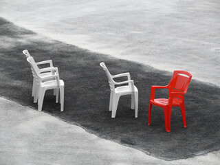 Three white chairs and one red on dark asphalt