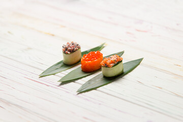 Set of Japanese Gunkan Maki Rolls: Sake with salmon caviar, tuna Maguro and salmon in cucumber served on bamboo leaves. Pan Asian dish on wooden board. Expensive raw seafood Asian restaurant menu
