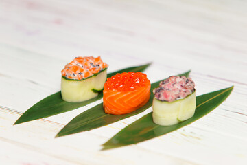 Set of Japanese Gunkan Maki Sushi Rolls. Sake nigiri with salmon and tobiko roe. Gunkan with salmon caviar.  Maguro in cucumber with tuna and flying fish roe eggs. served on green bamboo leaves.
