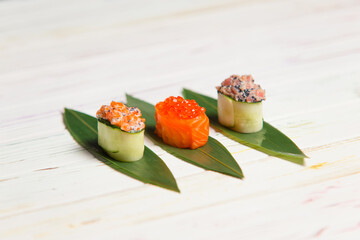 Set of Japanese Gunkan Maki Sushi Rolls: Sake with salmon caviar, tuna Maguro and salmon in cucumber served on bamboo leaves. Pan Asian dish on wooden board. Expensive seafood restaurant meal close up