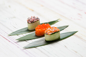 Set of Japanese Gunkan Maki Sushi Rolls: Sake with salmon caviar, tuna Maguro and salmon in cucumber served on bamboo leaves. Pan Asian dish on wooden board. Expensive seafood Asian restaurant menu
