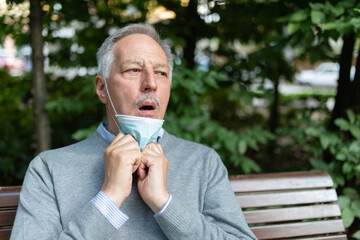Man having difficulty to breath with his mask on, coronavirus prevention in summer concept