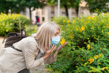 Woman trying to smell flower while wearing a mask, coronavirus pandemic concept