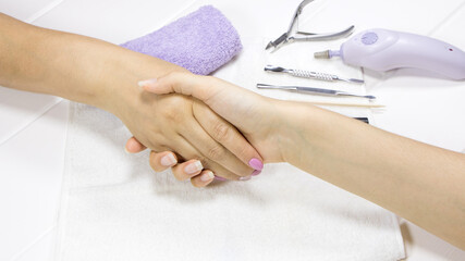 Women manicurist and client shake hands in the salon for the care of hands and nails. A woman greets a customer. Beauty salon. Thank you for a job well done. Close-up handshake, pink manicure.