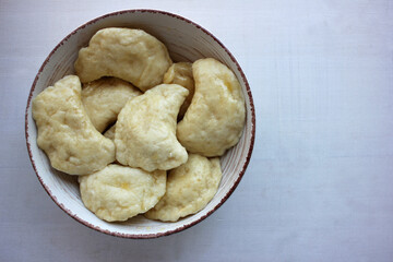 Home-cooked dumplings with cottage cheese in a vintage bowl on white wooden background. Top view. Cooking at home concept. Selective focus