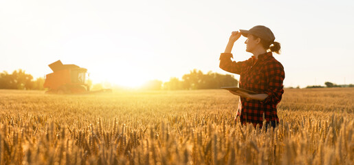 Woman farmer with digital tablet on a background of harvester. Smart farming concept.	
