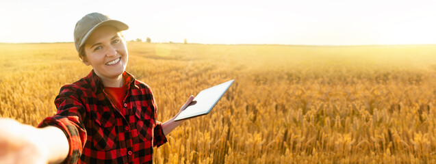 Woman farmer with digital tablet makes selfie on the background of a wheat field.	