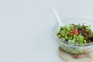 fresh vegetable salad tomatoes, cucumbers, lettuce leaves, pine nuts, walnuts in a glass plate with a white spoon on a wooden stand on a white background and there is a place for the inscription 