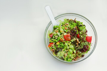 fresh vegetable salad tomatoes, cucumbers, lettuce leaves, pine nuts, walnuts in a glass plate with a white spoon on a wooden stand on a white background