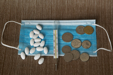 Obraz na płótnie Canvas disposable medical mask, white tablets, mercury thermometer and coins. The concept of cost of health