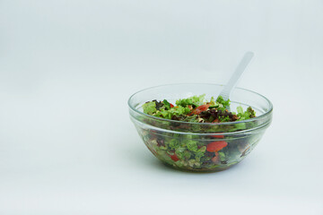 fresh vegetable salad tomatoes, cucumbers, lettuce leaves, pine nuts, walnuts and seeds in a transparent large plate with a white spoon on a white background