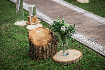 Vases with floral arrangements along the path to the arch at a Jewish wedding ceremony next to sections of tree trunks in a rustic style.