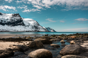 Pebble norwegian beach, less sea, beautiful blue water, snowy mountains. Arctic landscape, Senja island, Norway. Horizontal orientation.