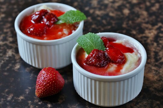 Pudding from semolina in the form of "ramekin" for baking with strawberry syrup and strawberries. On a dark background. Soft focus. copy space