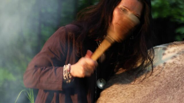 Female shaman performs a shamanic rite with a tambourine by the fire in the forest
