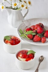 Pudding from semolina in the form of "ramekin" for baking with strawberry syrup and strawberries on a white tablecloth. daisies in a white pitcher. Soft focus