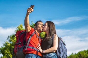 Naklejka premium Couple of hikers in the mountains kissing taking a photo with the mobile