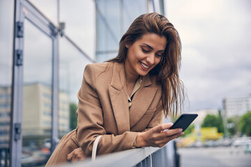 Contented fashionable woman staring at her smartphone