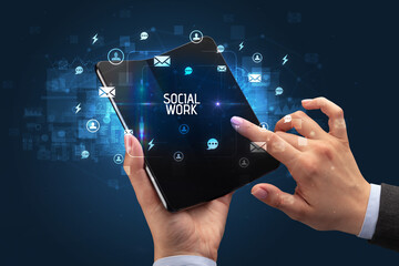 Businessman holding a foldable smartphone with SOCIAL WORK inscription, social networking concept