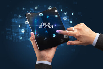 Businessman holding a foldable smartphone with SOCIAL STRATEGY inscription, social networking concept