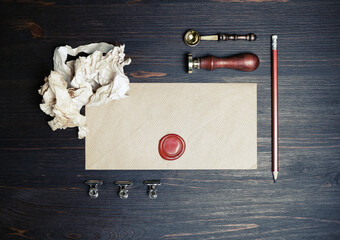 Blank kraft paper envelope with wax seal, stamp, spoon, pencil and crumpled paper on vintage wooden...