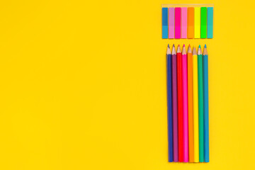 Back to school. Colored pencils and stickers on a yellow background. Top view, horizontal position, space for text. Layout for the designer