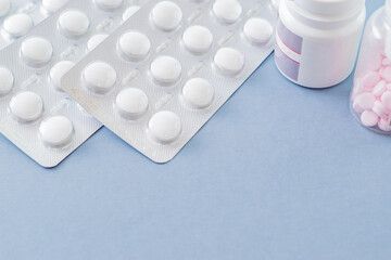 White pills in a blister and pills in a bottle on a blue background. Medical pharmacy concept