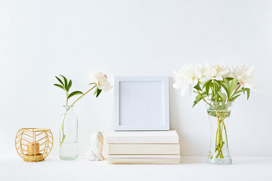 Home interior with decor elements. White frame, white peonies in a vase, interior decoration