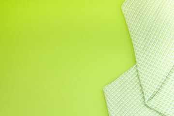 Light green kitchen towel in a cage, on a green background. Top view, space for text, horizontal position. Concept of kitchen equipment.