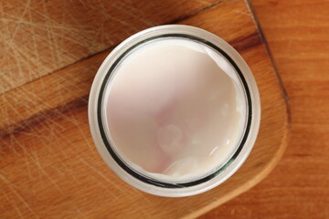 Fototapeta na wymiar Yogurt in open small glass jar on wooden cutting board. Directly Above.
