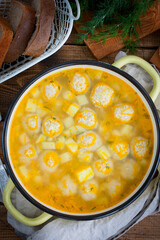 Potato soup with meatballs in an enameled pan on a wooden table, selective focus