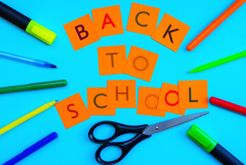School concept: cut out of paper letters" BACK to SCHOOL " are on a blue background, along the edges of pens, markers and scissors. Top view, close-up, horizontal position