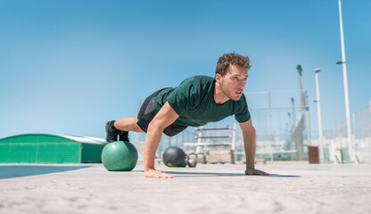 Fit exercises man strength training core doing balance push-ups workout at outdoor gym balancing on stability medicine ball with legs. Bodyweight pushups exercises. Push-up variation.