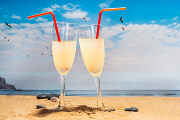 two cocktail glasses with straws on the beach with seagulls flying