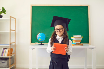 Back to school. A cute schoolgirl in a graduate hat with books stands against the backdrop of a...