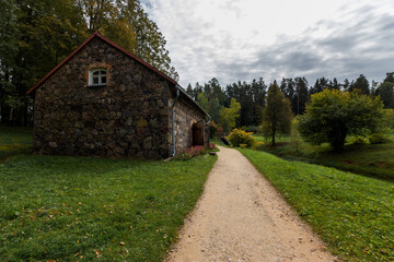 An old rustic stone barn for storing grain and grain near an earthen path on a clear summer day